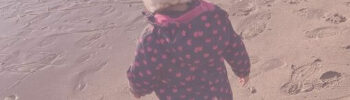 Beitragsbild Blogartikel Mit Stoffwindeln unterwegs - Kleines Mädchen in Regenkleidung und mit Mütze am Strand