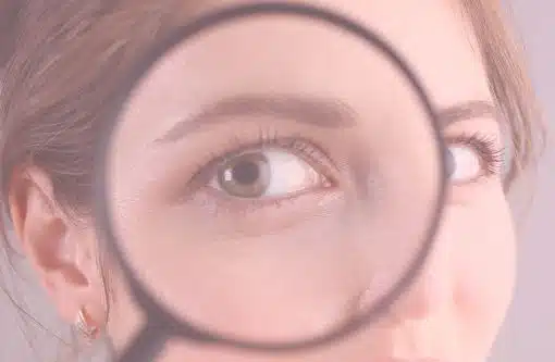 Halbes Gesicht einer Frau, die sich eine Lupe vor das Auge hält