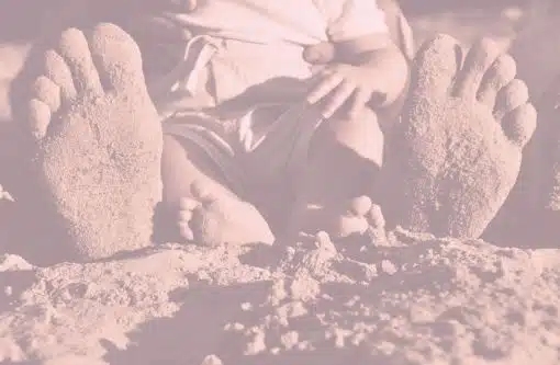 Füße eines im Sand sitzenden Babys