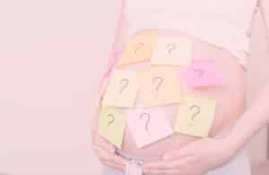 Schwangerschaftsbauch mit vielen bunten Klebezetteln mit Fragezeichen darauf