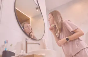 Frau schaut in den Spiegel und zeigt mit dem Finger auf eine Stelle im Gesicht