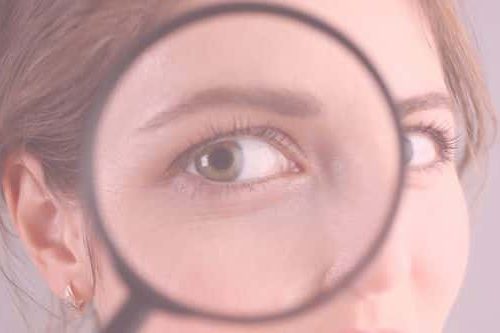 Halbes Gesicht einer Frau, die sich eine Lupe vor das Auge hält