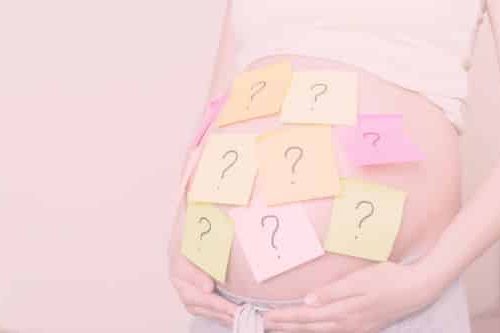 Schwangerschaftsbauch mit vielen bunten Klebezetteln mit Fragezeichen darauf